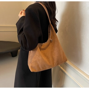 Détail d'un grand sac hobo en daim marron porté à l'épaule sur un manteau en laine noir