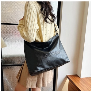 Side view of a black pebbled leather tote bag with FASHION embossed letters on a model