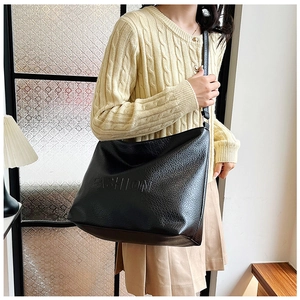 Detailed view of black pebbled leather tote bag with FASHION embossing and long strap
