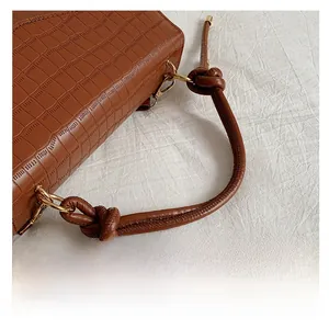Macro shot of brown crocodile embossed bag featuring a unique knotted handle and gold hardware