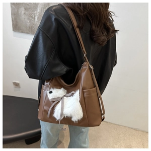 Dettaglio borsa a tracolla in pelle marrone con patch cucciolo di peluche e fiocco