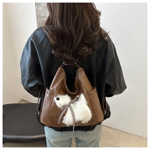 Dettaglio dello zaino in pelle marrone scuro con ciondolo a cucciolo di peluche su modella