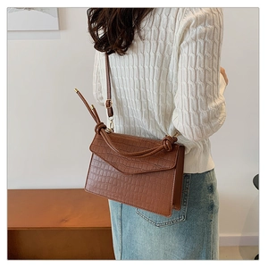 Brown crocodile pattern crossbody bag with V-shaped flap shown on a model