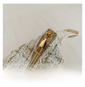 Macro view of light gold metal zipper and white tweed fabric with metallic gold thread
