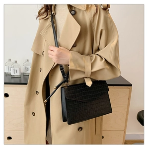 Black crocodile embossed square handbag with gold hardware styled on a beige trench coat