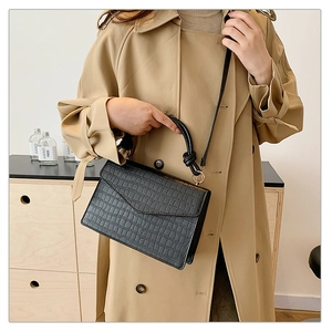 Chic black crocodile-embossed mini bag with unique knotted handle on khaki trench coat