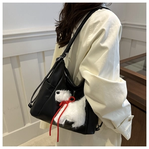 Dettaglio di borsa a spalla nera con un cucciolo di peluche bianco e nastro rosso