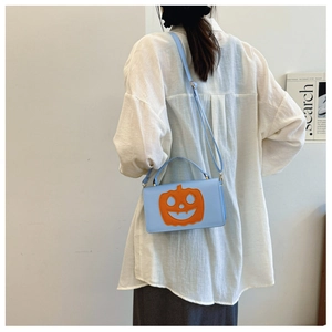 Close-up of light blue Halloween pumpkin square bag worn by model against a white wall
