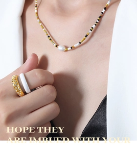 Detail of beaded pearl necklace and layered rings on model with chic black and white suit