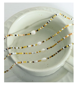 Detail of beaded necklace with freshwater pearl hanging on a white ceramic cup