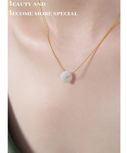 Gros plan d'un collier doré avec pendentif en jade blanc sur le cou d'une femme