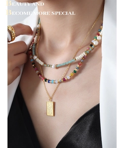 Close-up of layered necklaces with colorful tourmaline beads and gold engraved tag