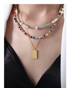 Close-up of a layered necklace featuring colorful tourmaline beads and an engraved gold tag