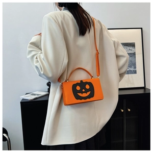 Detail of a bright orange Jack-o'-lantern handbag with golden metal hardware and strap