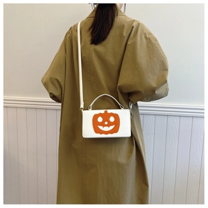 White Halloween crossbody bag with orange pumpkin face shown on a trench coat model