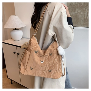 Detail of apricot pleated tote bag featuring silver butterfly rivets and plush ball charm