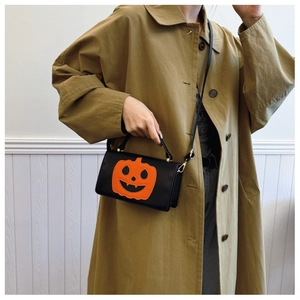 Detail of black pumpkin crossbody bag with orange embroidery worn with a trench coat