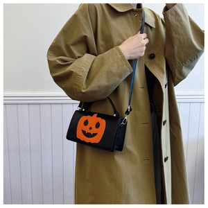 Close-up of Halloween crossbody bag with orange pumpkin face on green coat model