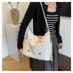 Detail of white nylon shoulder bag featuring golden butterfly charms and side pocket