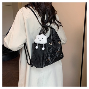 Détail d'un sac à dos plissé noir avec papillon doré et breloque nuage sur un manteau beige