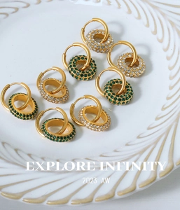 Close-up of double layer 18k gold hoop earrings with green crystals on white ceramic plate