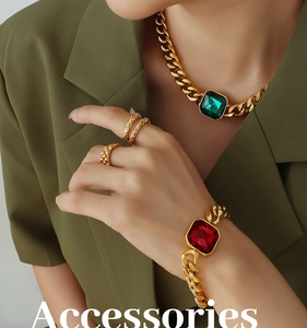 Dettaglio della collana a catena cubana dorata con pietra verde e bracciale con gemma rossa