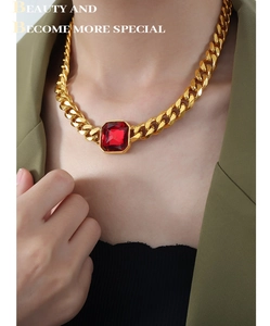 Collana a catena dorata con pendente in cristallo rosso quadrato indossata su blazer verde