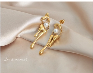 Detalle de pendientes de metal líquido dorado con perlas sobre seda champán