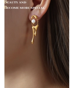 Detalle macro de pendientes de lava chapados en oro 18k con perla blanca y borla