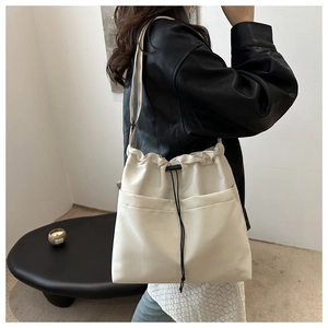 Detail of off-white drawstring bucket bag showing front pockets and nylon texture