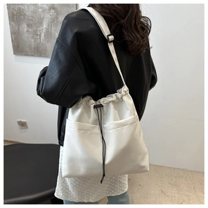 Detail of white drawstring bucket bag with dual front pockets and adjustable strap