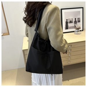 Detail of black large nylon tote bag with drawstring closure and two front pockets on model