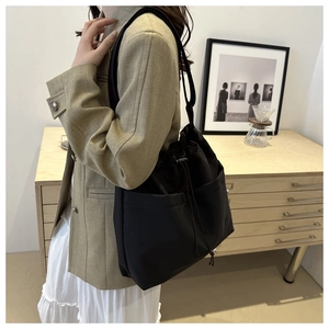 Black drawstring bucket bag with two front pockets in a minimalist interior setting