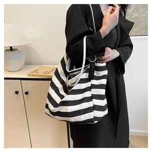 Close-up of a large black and white striped canvas tote bag worn with a black coat