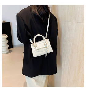 Detailed view of an off-white crossbody bag with zipper fringe on a black blazer