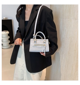Detail of light gray crossbody bag with zipper accent and long tassel on a model