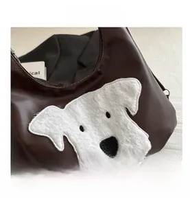 Detail of dark brown leather tote featuring a white plush dog patch and fine texture
