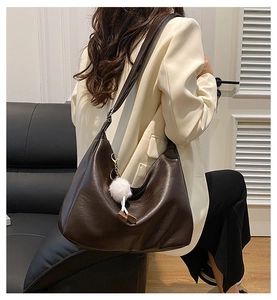 Detail of dark brown leather tote bag featuring a white plush charm on the shoulder strap