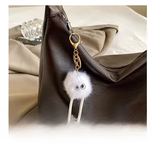 Close-up of white plush monster charm with big eyes on a dark leather tote bag
