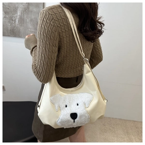 Detail of cream faux leather tote featuring a plush puppy patch and adjustable strap