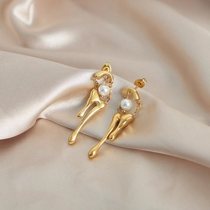 Pendientes largos dorados de forma fluida con perlas blancas sobre tela de seda champán