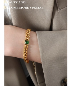 Detail of gold-plated Cuban chain bracelet with an emerald-cut green stone on wrist