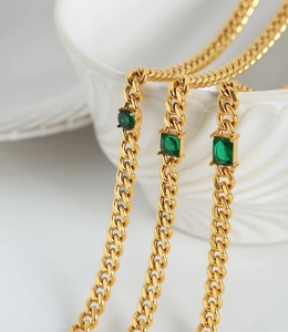 Detail of gold Cuban chain necklace with emerald green crystals on white ceramic edge