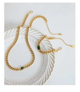 Detailed view of emerald zircon gold curb chain necklace and bracelet on white porcelain