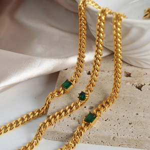 Gold Cuban link necklace with emerald green gemstones on premium stone background