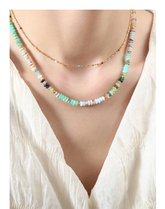 Detail of layered gold bead chain and colorful stone necklace on a white texture fabric