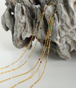 Detail view of gold bead chain with colorful beads over textured stone backdrop