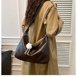 Detail of deep brown glossy leather tote bag with white faux fur charm and adjustable strap