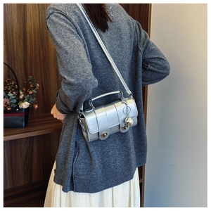 Detail of silver metallic crossbody bag with dual turn-lock and ball charm accessory