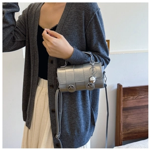 Detail of silver metallic textured crossbody bag with dual turn-lock and ball charm